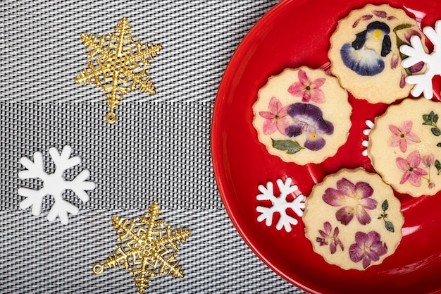 Foto vista superior de hermosas galletas de flores comestibles con copos de nieve de adorno de navidad en una placa de color rojo brillante