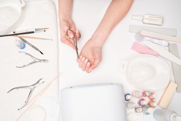 Vista superior de herramientas de manicura y mujer preparando sus manos para el procedimiento de manicura