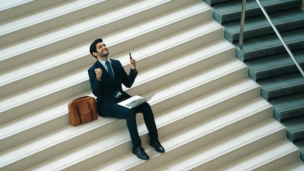 Vista superior de un hombre celebrando un proyecto exitoso mientras está sentado en las escaleras exultante