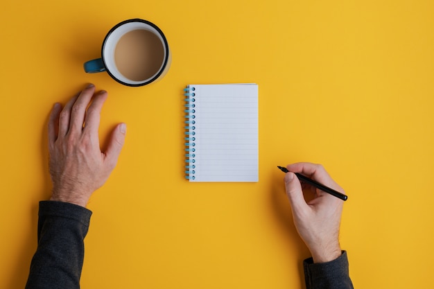 Vista superior de un hombre listo para escribir en su bloc de notas en blanco con marcador negro