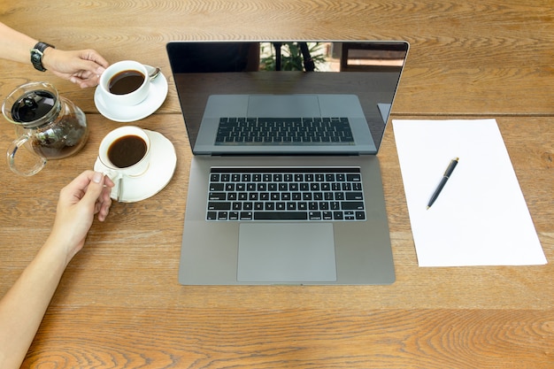 La vista superior del hombre de negocios da sostener la taza de café con el ordenador portátil en la tabla.