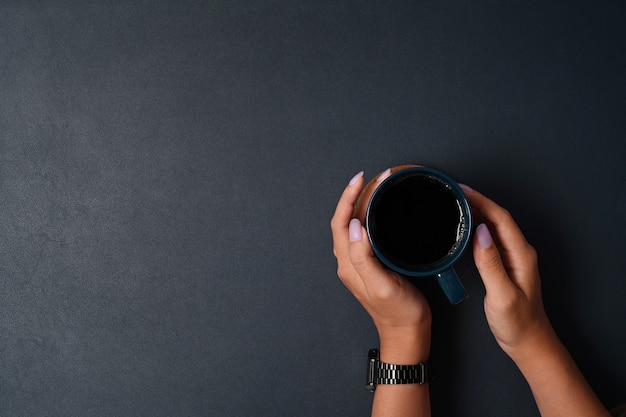 Vista superior del hombre que sostiene una taza de bebida caliente en cuero negro.