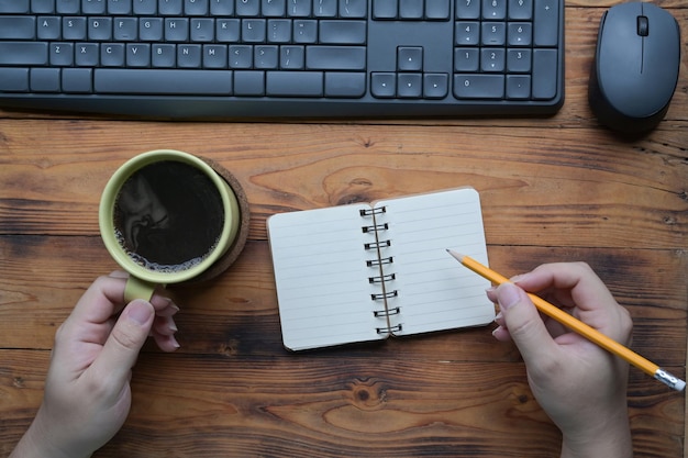 Vista superior del hombre que sostiene la taza de café y toma nota en el cuaderno