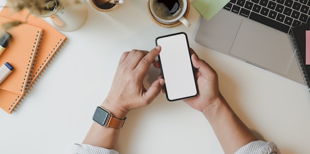 Vista superior del hombre que sostiene el teléfono inteligente de pantalla en blanco en un lugar de trabajo mínimo