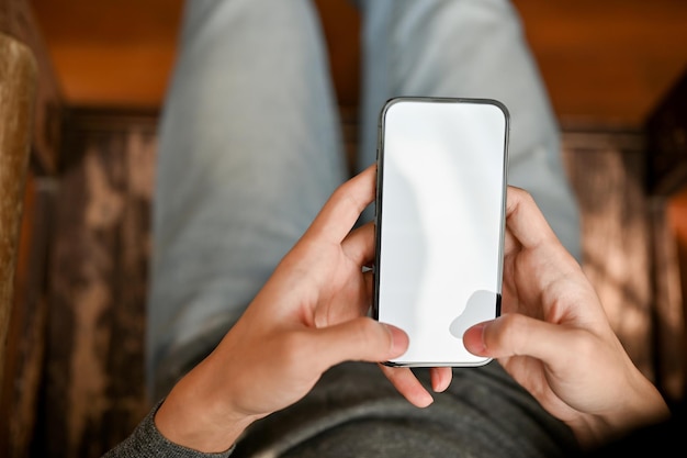 Vista superior de un hombre que usa su teléfono móvil inteligente mientras está sentado en la maqueta del teléfono inteligente de su habitación