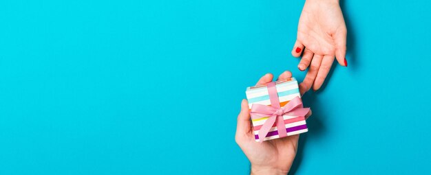 Foto vista superior de un hombre sosteniendo y dando un regalo a una mujer en un fondo colorido recibiendo un regalo