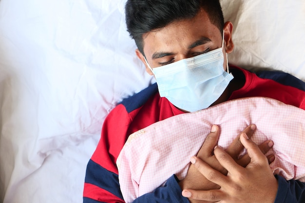 Vista superior de hombres enfermos con mascarilla quirúrgica en la cama poniendo la mano en el pecho.