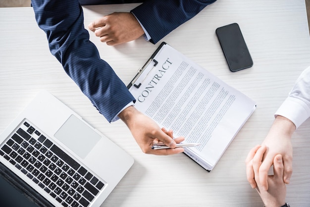 Vista superior de hombres de negocios en ropa formal sentados en el escritorio con contrato, concepto de negocio