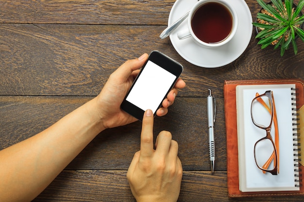 Vista superior homem de negócios usando telefone celular e caneta, caderno, óculos, cactos no fundo de mesa de escritório de madeira.