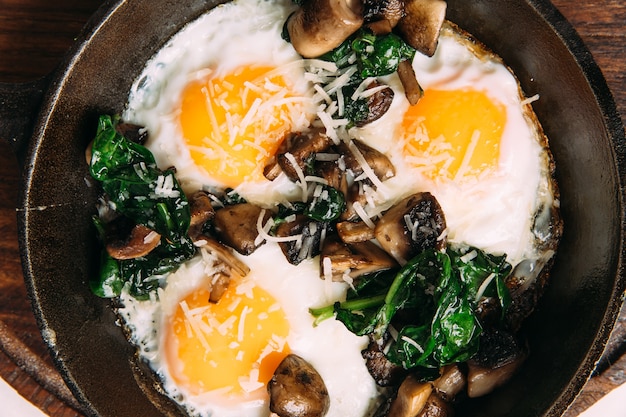 Vista superior de huevos fritos con champiñones y espinacas en sartén de hierro fundido