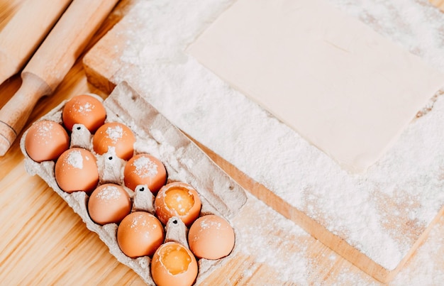 Vista superior de huevos de gallina en masa de hojaldre de cartón en una tabla de cortar dragada con harina de trigo para hornear pan de galleta