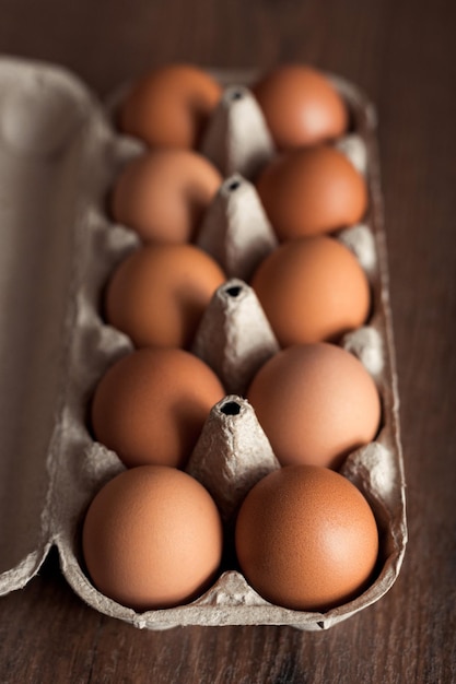 Vista superior de huevos de gallina naturales y orgánicos en caja de papel artesanal sobre mesa de madera marrón