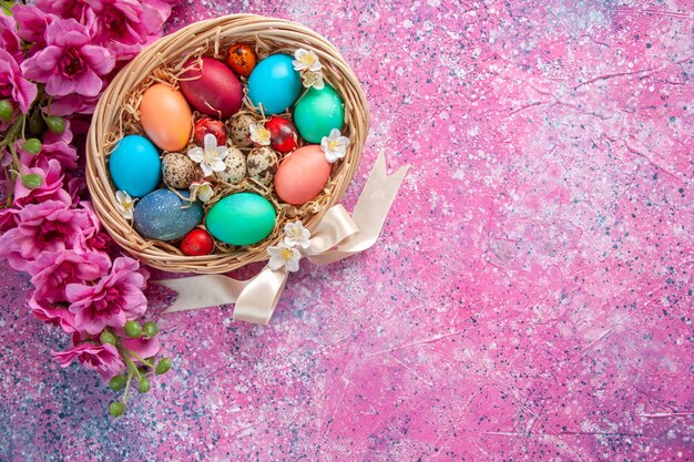 Vista superior de los huevos de pascua de color dentro de la canasta en la superficie rosada primavera colorido concepto de vacaciones de pascua color ornamentado