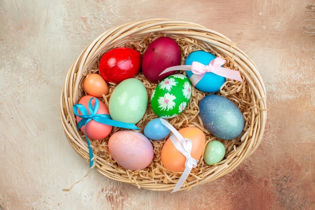 Vista superior de los huevos de pascua de colores algunos atados con lindos arcos dentro de la canasta sobre una superficie clara