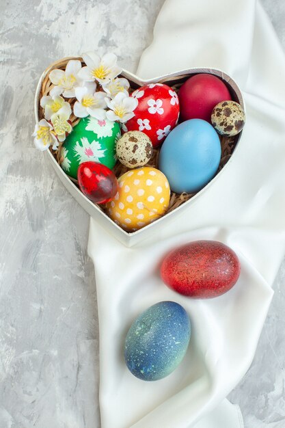 Vista superior de huevos de pascua de colores dentro de la caja en forma de corazón sobre una superficie blanca