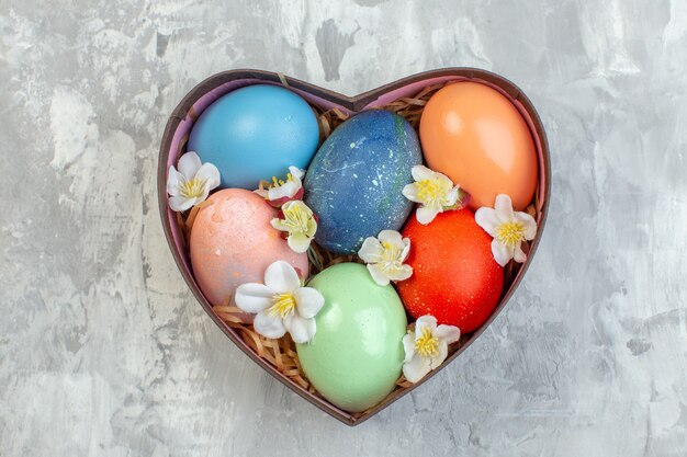 Vista superior de huevos de pascua de colores dentro de la caja en forma de corazón sobre una superficie blanca