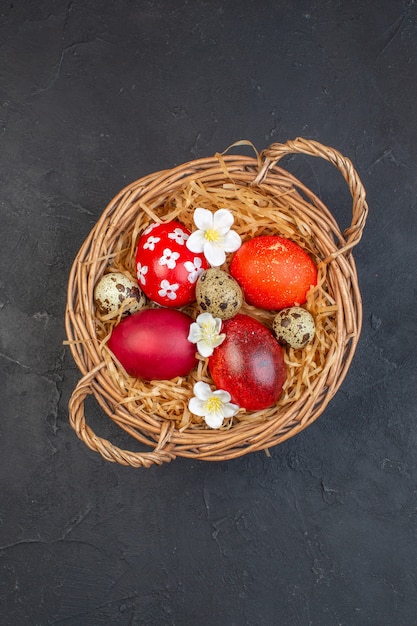 Vista superior de los huevos de pascua de colores dentro de la canasta sobre una superficie oscura