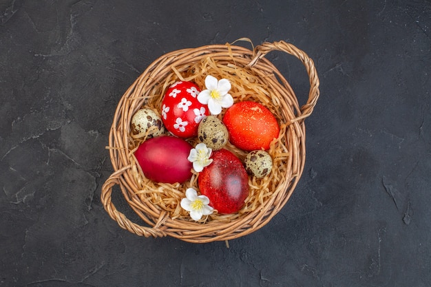 Vista superior de los huevos de pascua de colores dentro de la canasta sobre una superficie oscura