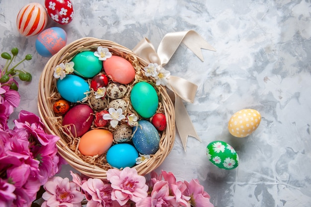 Vista superior de los huevos de pascua de colores dentro de la cesta sobre la superficie blanca primavera coloridas flores de pascua concepto ornamentado de vacaciones
