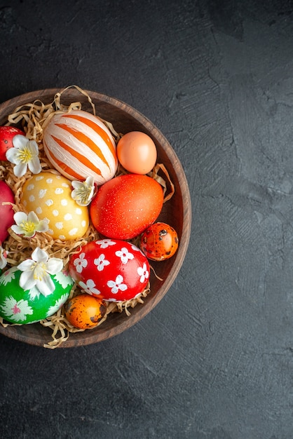 Vista superior de huevos de pascua de colores dentro de la placa marrón sobre una superficie oscura