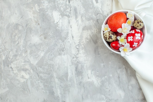 Vista superior de huevos de pascua de colores dentro de la taza blanca sobre la superficie blanca