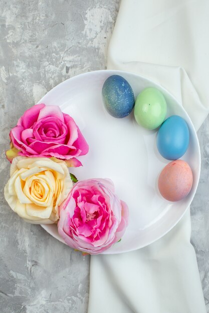 Vista superior de huevos de pascua de colores con flores dentro de la placa sobre la superficie blanca