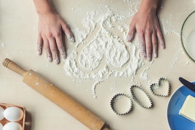 Vista superior de la imagen recortada de la niña haciendo corazón de harina mientras hornea