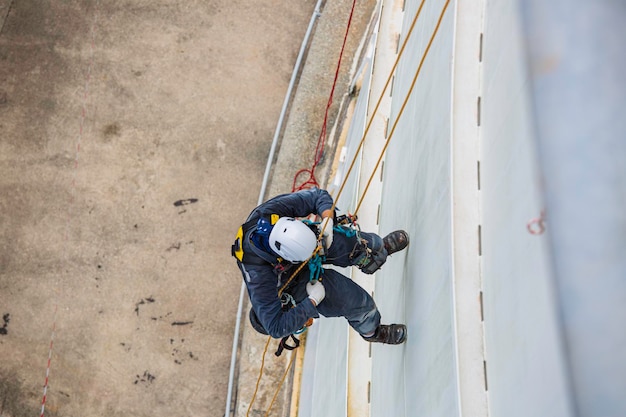 Vista superior de la inspección del trabajador masculino que usa la primera línea de seguridad de la cuerda del arnés de seguridad que trabaja en un lugar alto en el techo del tanque esférico