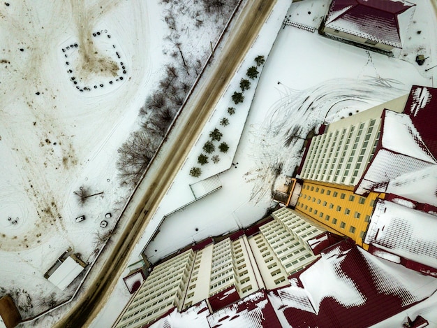 Vista superior de invierno aérea del moderno edificio de apartamentos grande en el área del suburbio en el camino estrecho y sucio y campo nevado.