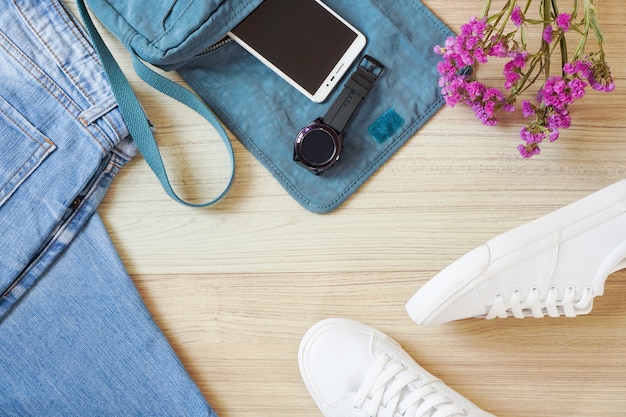 Vista superior de jean, teléfono móvil, reloj inteligente y zapatillas blancas como moda streetwear de niña