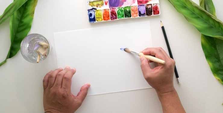 Foto vista superior del joven artista profesional pintando sobre papel de dibujo con acuarela