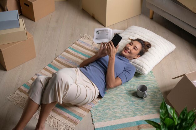 Foto vista superior de una joven asiática relajándose en una casa nueva acostada en el suelo usando un teléfono inteligente después de mudarse