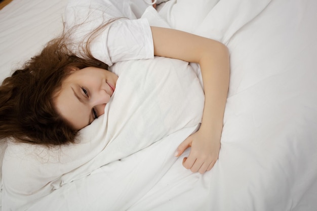 Vista superior de una joven atractiva casi durmiendo en la cama abrazando a una adolescente con una suave almohada blanca