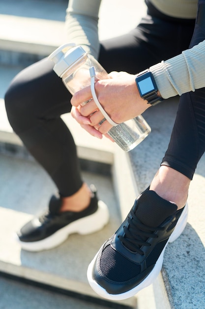 Vista superior de una joven deportista con leggins negros y zapatillas sosteniendo una botella