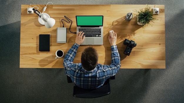 Vista superior de un joven fotógrafo procesando fotografías en su portátil con cámara de pantalla verde, disco duro externo y portátil a su lado