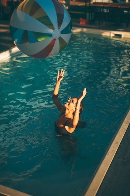 Vista superior a la joven mujer con pelota en la piscina en un día soleado