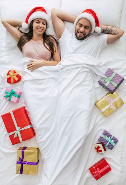 Vista superior de la joven pareja con gorro de Papá Noel sentado en la cama