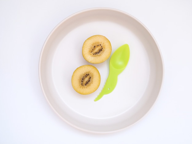 Vista superior del kiwi dorado con una cuchara de plástico verde en un plato redondo, limpie los alimentos con frutas de dieta para una buena salud.