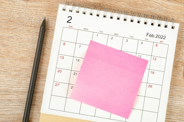 Vista superior del lápiz, planificación de calendario y fecha límite con nota adhesiva sobre fondo de madera, escritorio de calendario 2022 en el mes de febrero