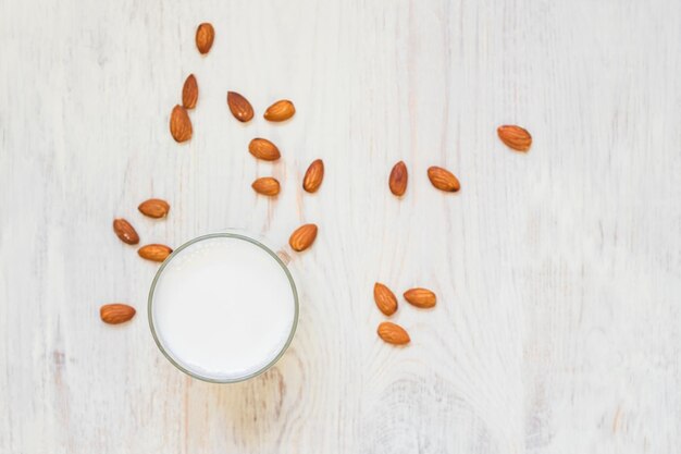 vista superior de leche de almendra casera en un vaso y nueces esparcidas en el espacio de copia de fondo de madera