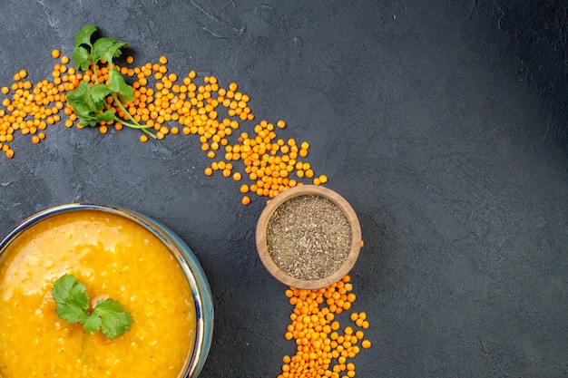 Vista superior de lentejas rojas alineadas en un círculo y deliciosa sopa de pimiento sobre fondo negro con espacio libre