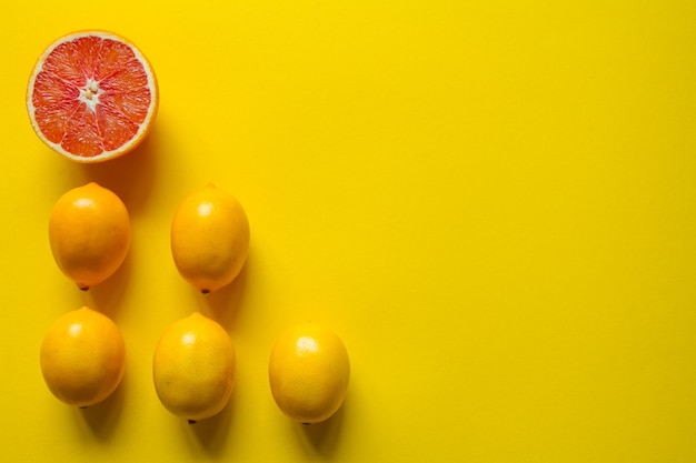 Vista superior de limón y pomelo maduro entero y en rodajas en varias filas sobre una superficie amarilla, concepto de salud y vitaminas