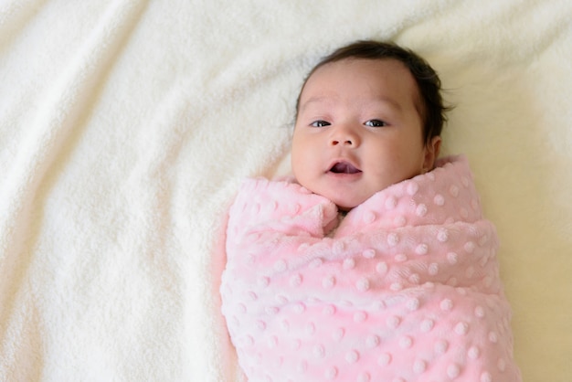 Vista superior de una linda niña asiática envuelta en un paño rosa en la cama