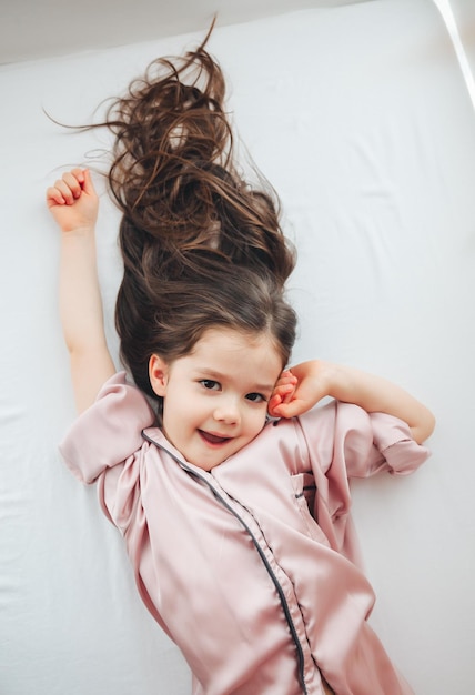 Vista superior de una linda niña que se estira en una cama blanca despertándose por la mañana El concepto de ir a la cama despertándose y relajándose