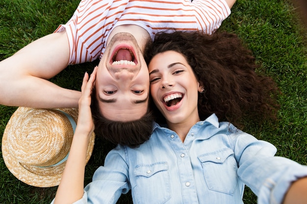 Foto vista superior de la linda pareja acostada junto a las cabezas opuestas sobre la hierba verde en el parque