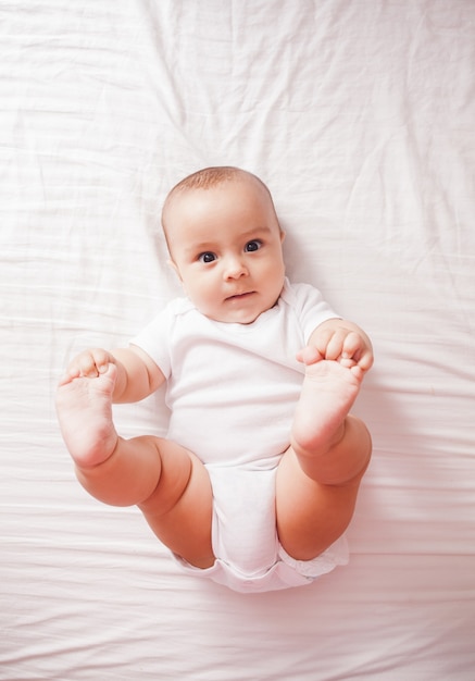 Vista superior de un lindo bebé acostado en una cama con los pies levantados