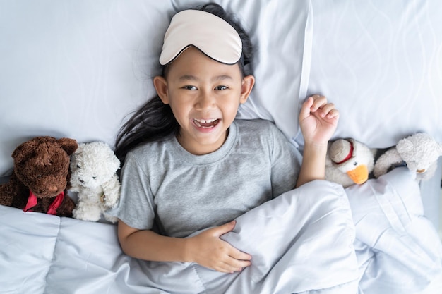 Vista superior lindo niño asiático niña se despierta y se acuesta en la cama con un oso de peluche de juguete