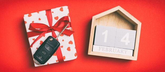Vista superior de la llave del coche en una caja de regalo con corazones rojos y calendario festivo sobre fondo de colores. El catorce de febrero. Presente para el concepto de San Valentín.