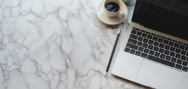 Vista superior del lugar de trabajo moderno y elegante con computadora portátil y una taza de café en la mesa de mármol