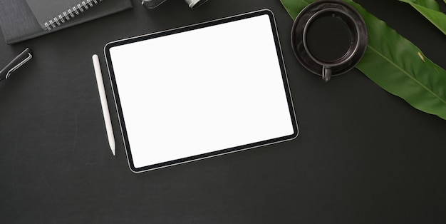 Vista superior del lugar de trabajo moderno oscuro con tableta digital de pantalla en blanco con material de oficina en mesa negra